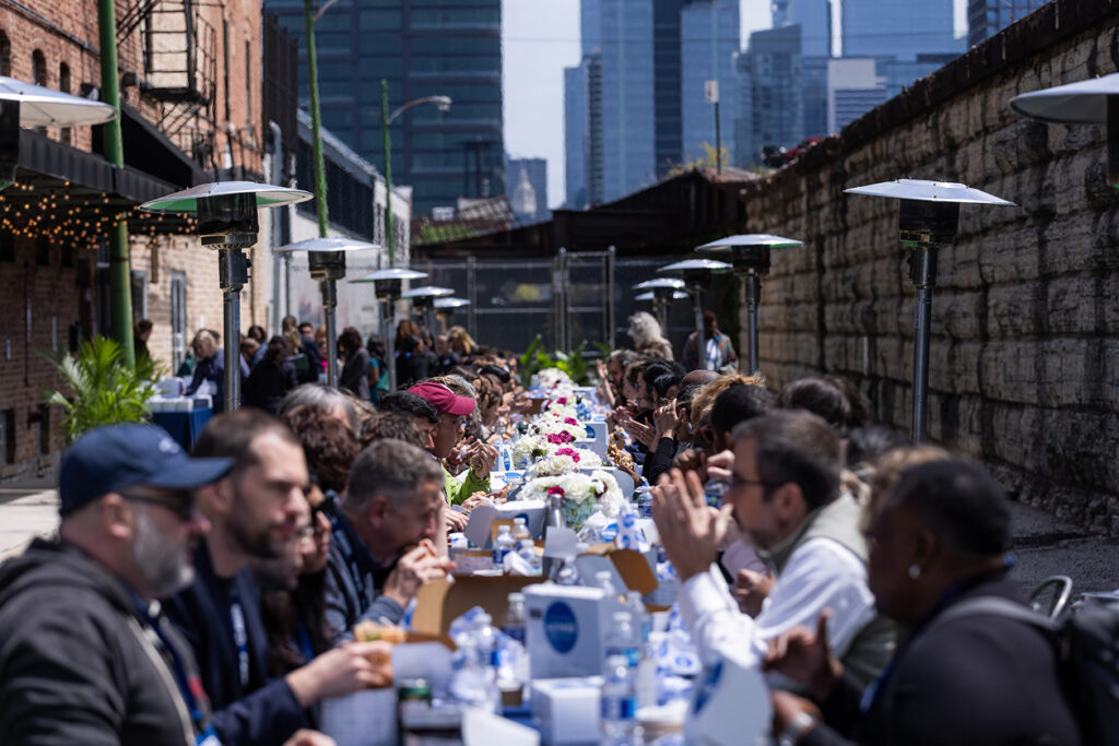 Long communal lunch table set up in a narrow outdoor alley with people seated and eating together.