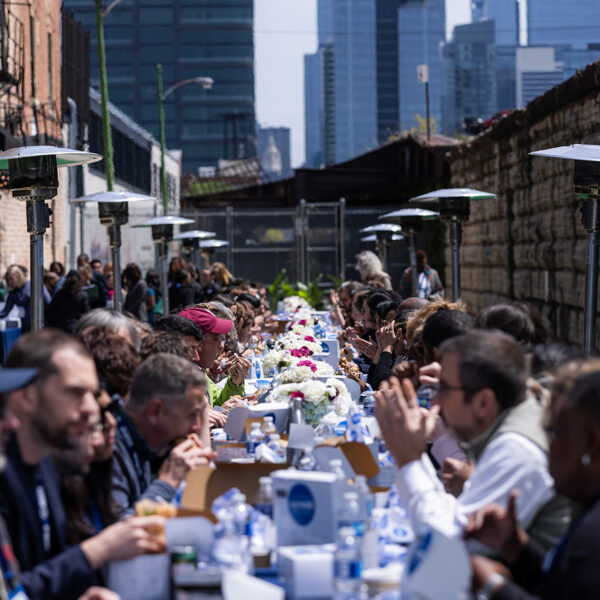 Long communal lunch table set up in a narrow outdoor alley with people seated and eating together.