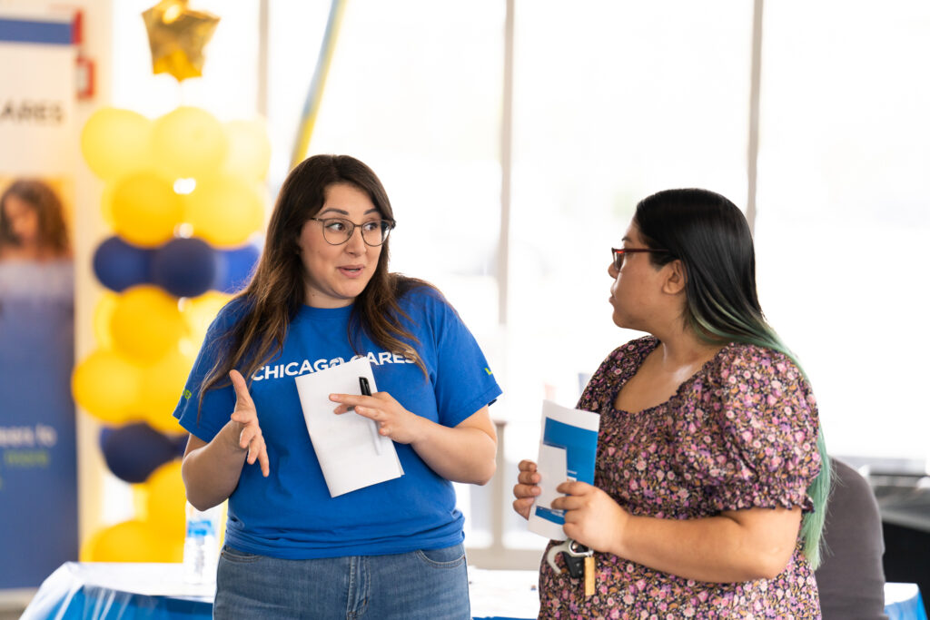 Two women talking at an indoor event; one wears a Chicago Cares shirt.