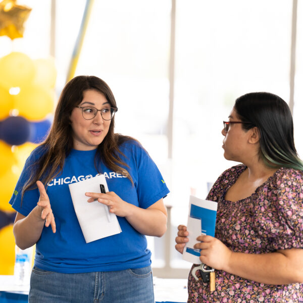 Two women talking at an indoor event; one wears a Chicago Cares shirt.
