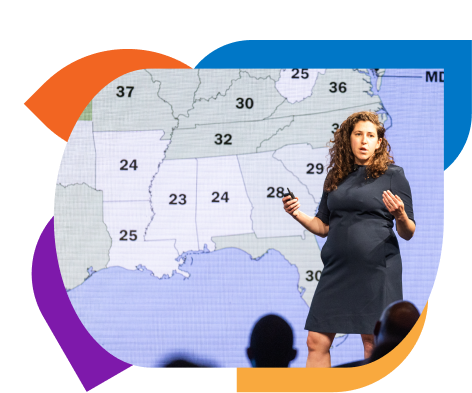 Presenter on stage pointing to a U.S. map with numbered markers during a talk.